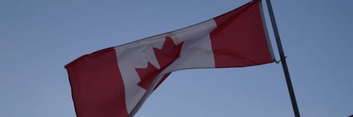 A Canadian flag billows in the breeze, hanging on a flag pole in front of a blue sky. (Mike McCulloch | Sovereign Canada) 